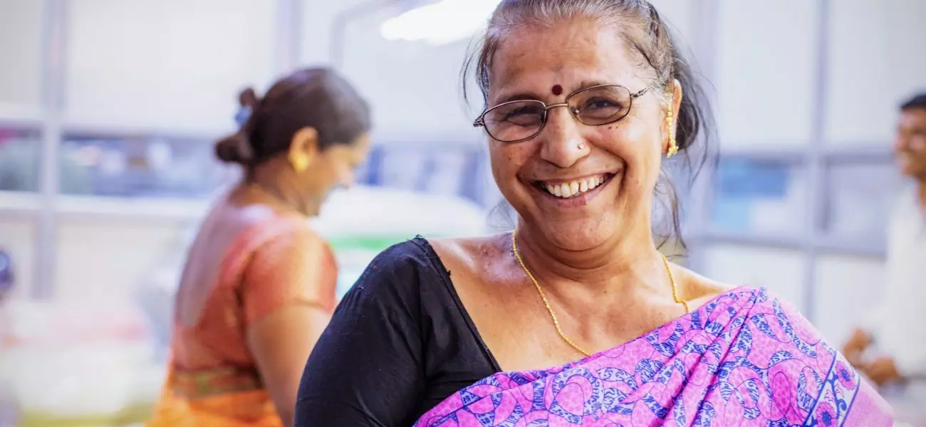 Factory, Worker, Textile Industry - A cheerful female factory worker at the Camera for a Portrait while her coworkers are working the background