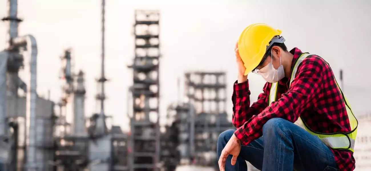 Unemployed concept from coronavirus or covid 19 crisis. Engineer asian man wearing yellow safety helmet, goggle and face mask sitting sad outside factory because of his lay-off. Unemployment crisis.