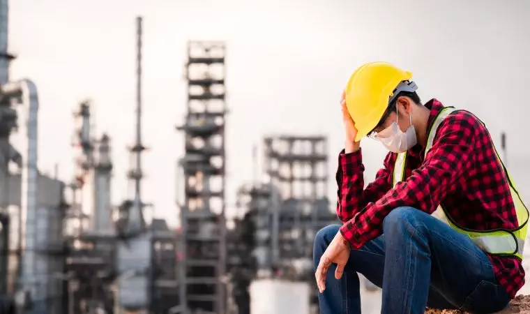 Unemployed concept from coronavirus or covid 19 crisis. Engineer asian man wearing yellow safety helmet, goggle and face mask sitting sad outside factory because of his lay-off.