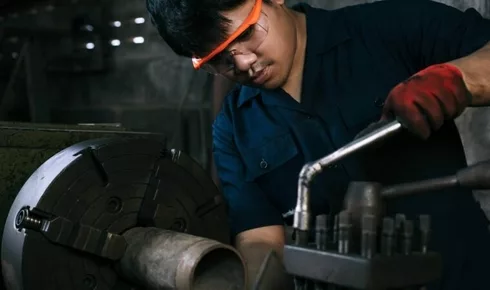 Diverse Asian manufacturing engineer using a socket hand tool to adjust industrial lathe equipment in factory workshop